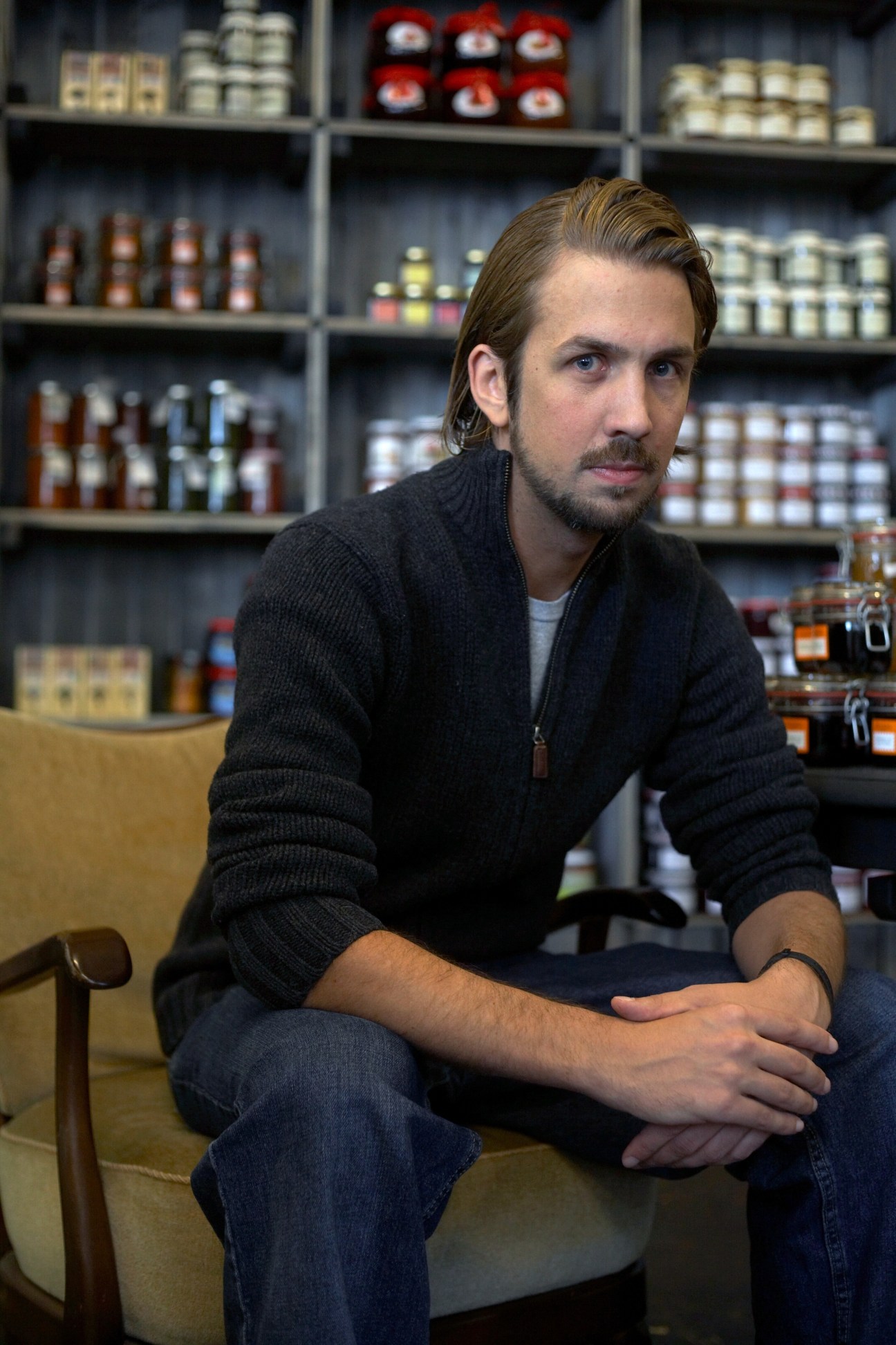 Jan Schawe, owner of Mutterland deli, sitting in front of shelves of jars and products.