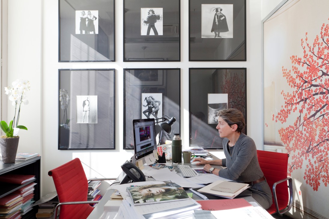 Woman working at desk in Vogue office surrounded by fashion photography and design materials.