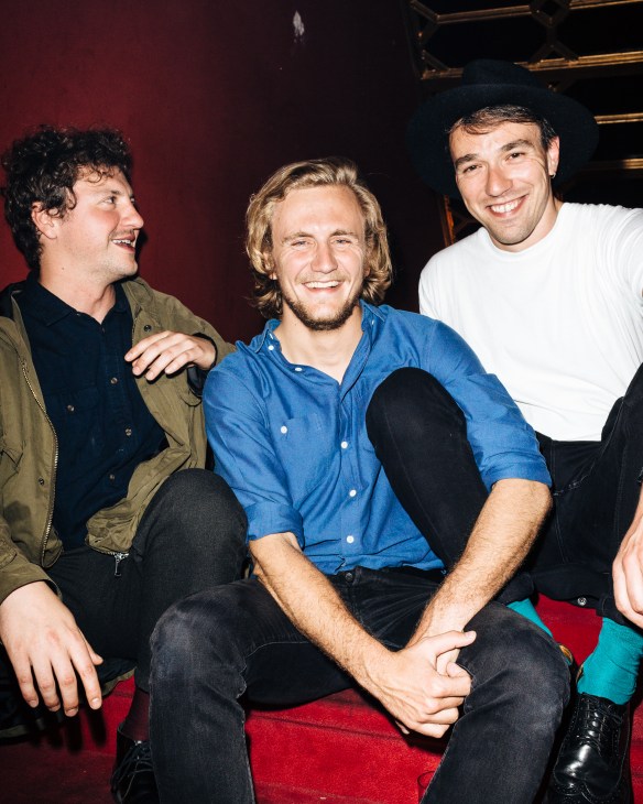 Three young men smiling and socializing against a red velvet wall at ChaChá nightclub in Madrid.