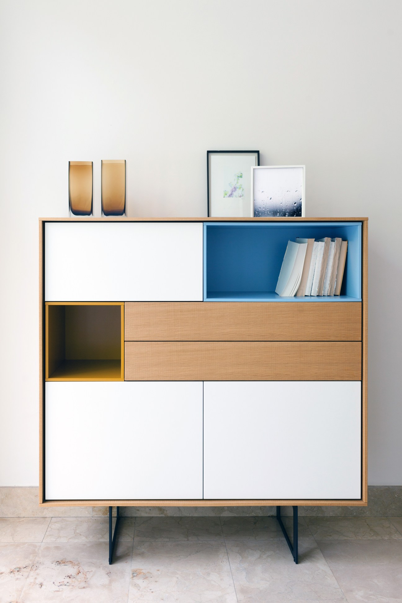 Wooden cabinet with white and blue panels, yellow accents, and dark metal legs displaying books and decorative items.