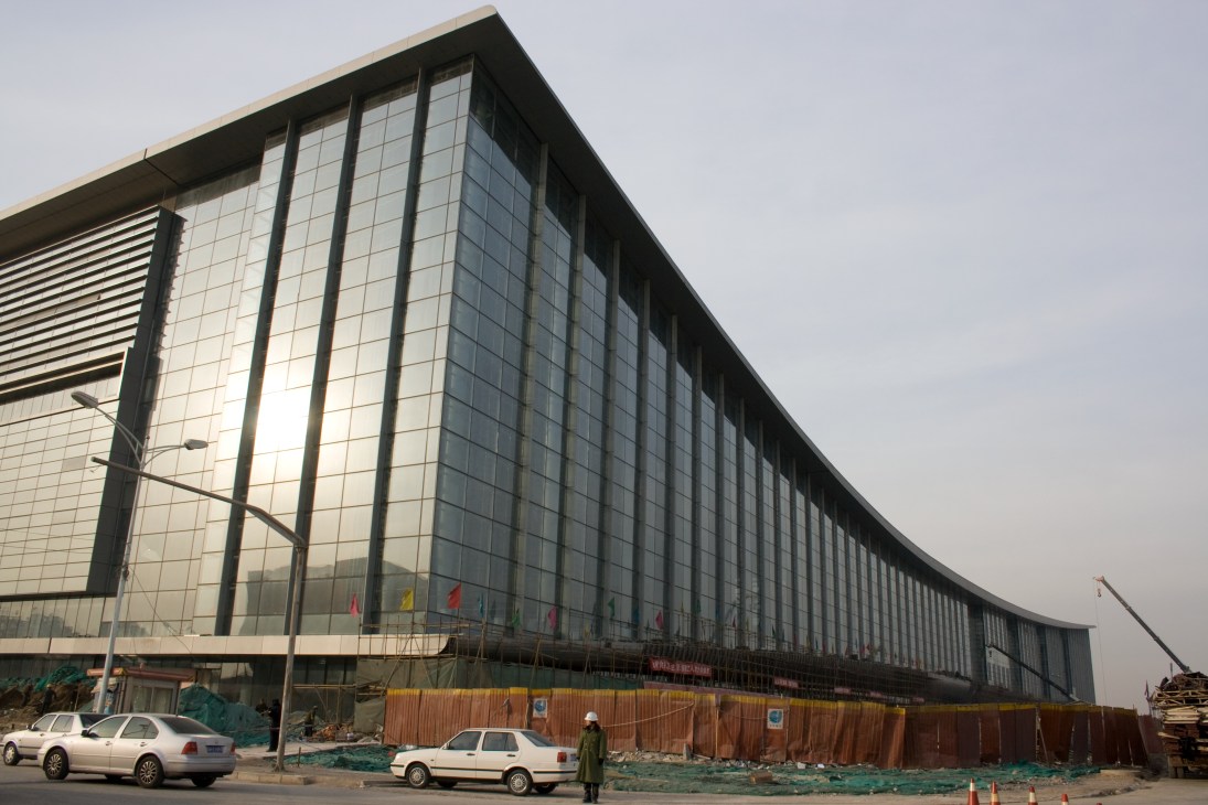 The National Convention Centre in Olympic Park, a large modern glass and steel building under construction with temporary fencing.