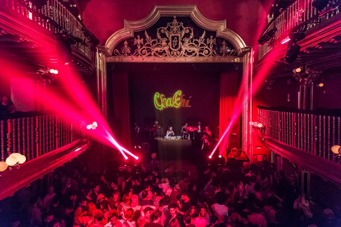 Interior of ChaChá nightclub with red lighting, ornate balconies, DJ booth with neon sign, and crowded dancefloor.