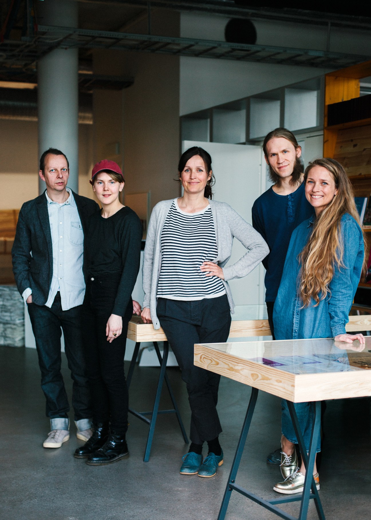Five people pose inside a modern gallery space with industrial architecture and wooden furniture.