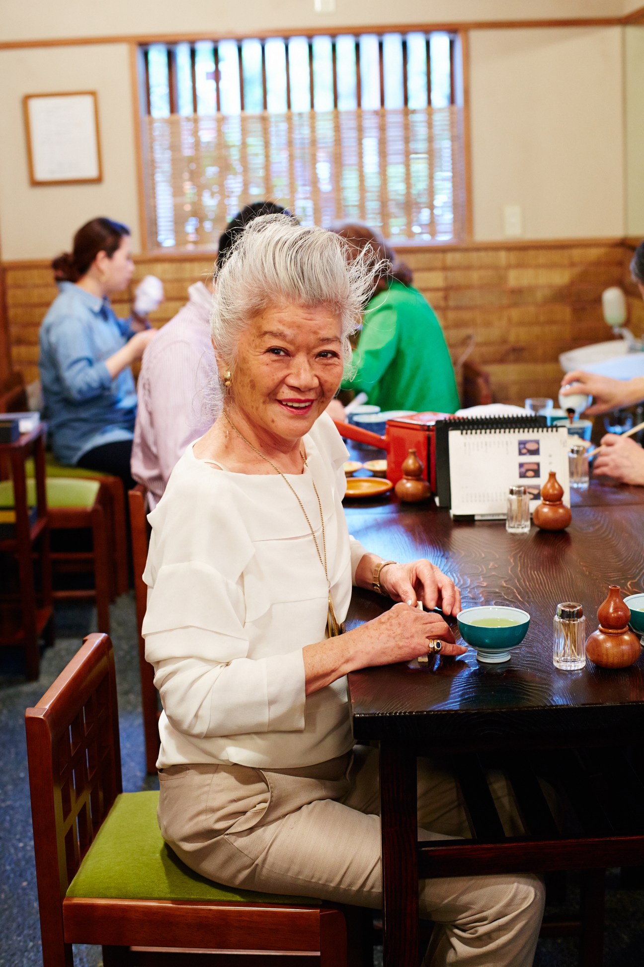 Fashion designer Junko Shimada seated at a table in a traditional Japanese restaurant interior.