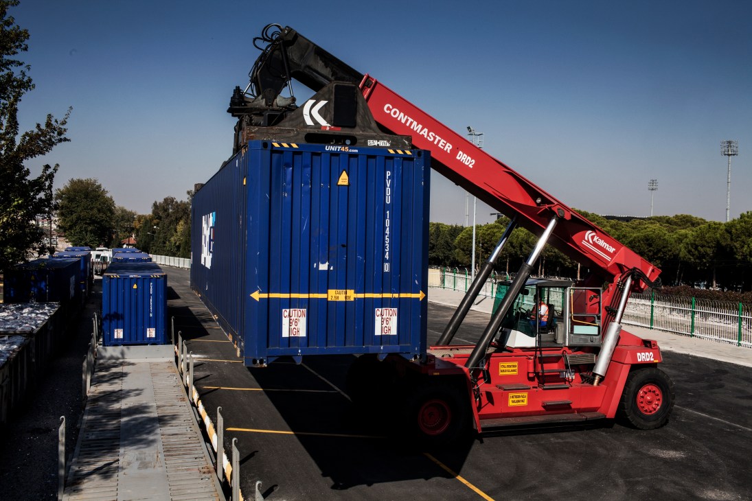 A red container crane lifts a blue freight container marked UNITAS at a railway depot.