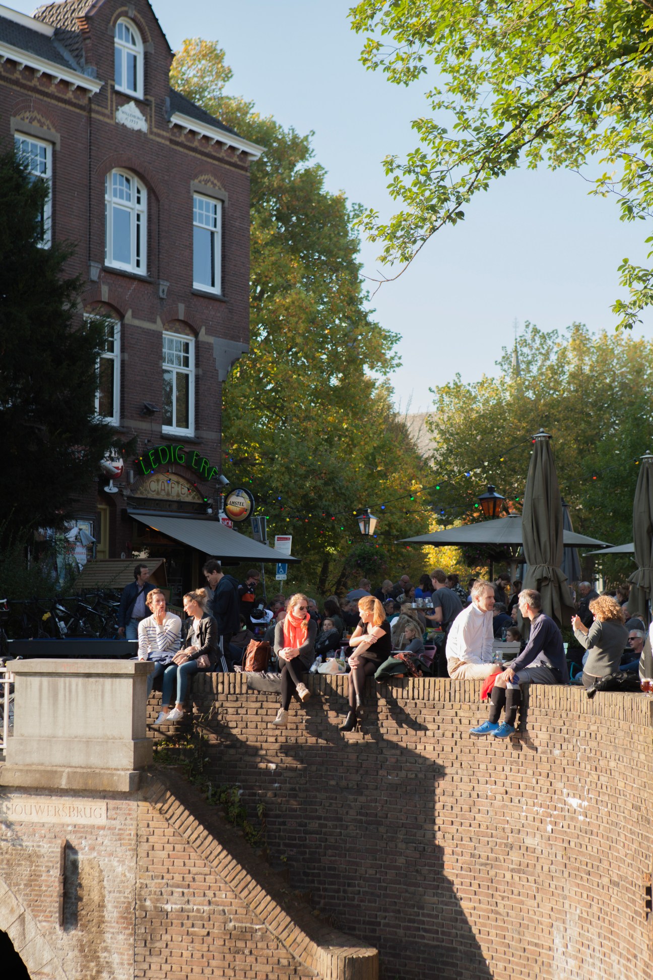 People sitting outside a brick building with a café on a terrace overlooking a canal in Utrecht