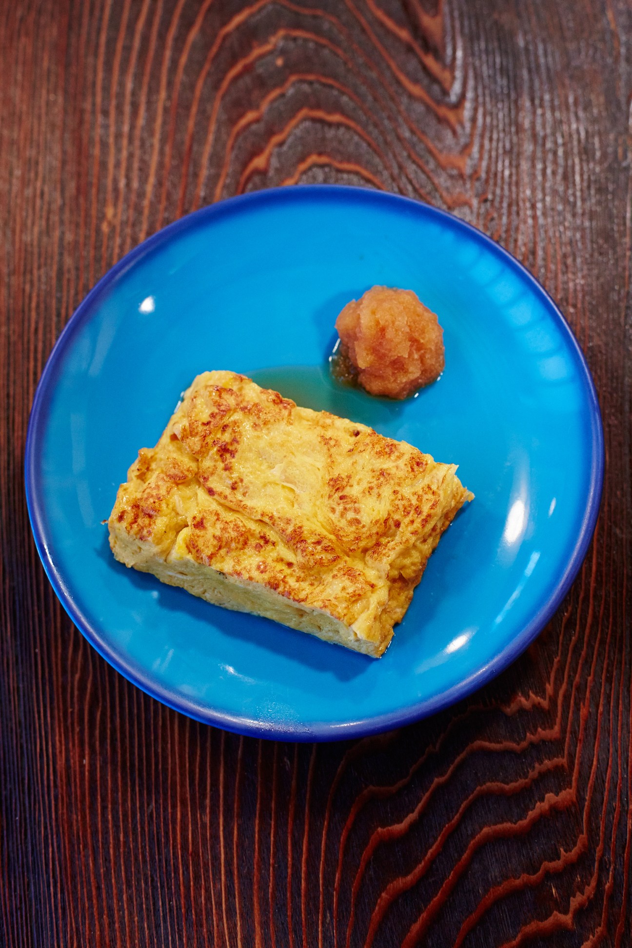 Tamagoyaki rolled omelette dusted with red spice and a golden fried ball on a bright blue plate.