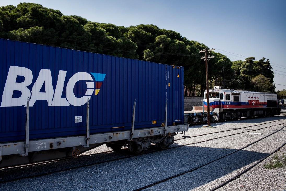 A blue BALO freight container on a railway wagon next to a red and white locomotive at Manisa loading point.