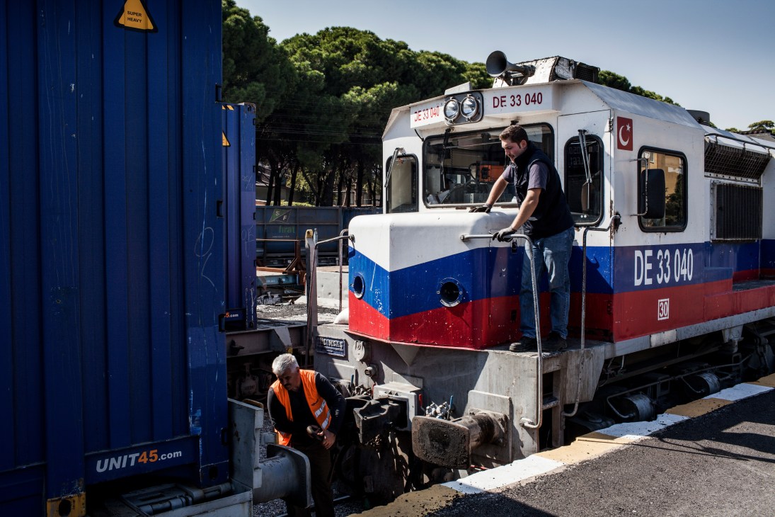Workers coupling a locomotive numbered DE 33 040 to blue freight containers at a rail depot.