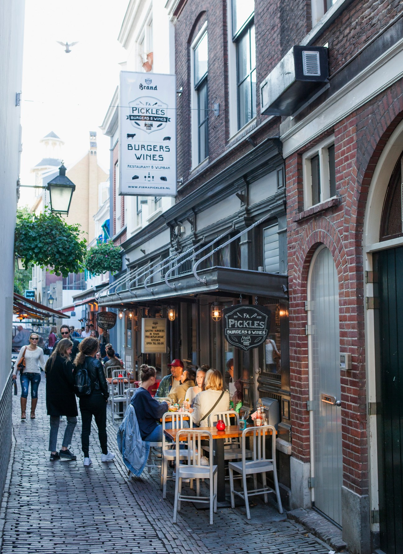 Firma Pickles burger restaurant with outdoor seating on a busy Utrecht street lined with historic brick buildings.