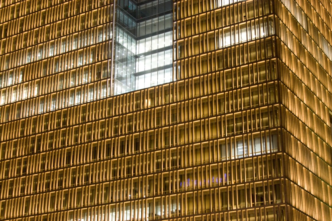 Golden-hued facade of Poly Plaza building in Beijing with repetitive vertical slat pattern and illuminated interior windows.