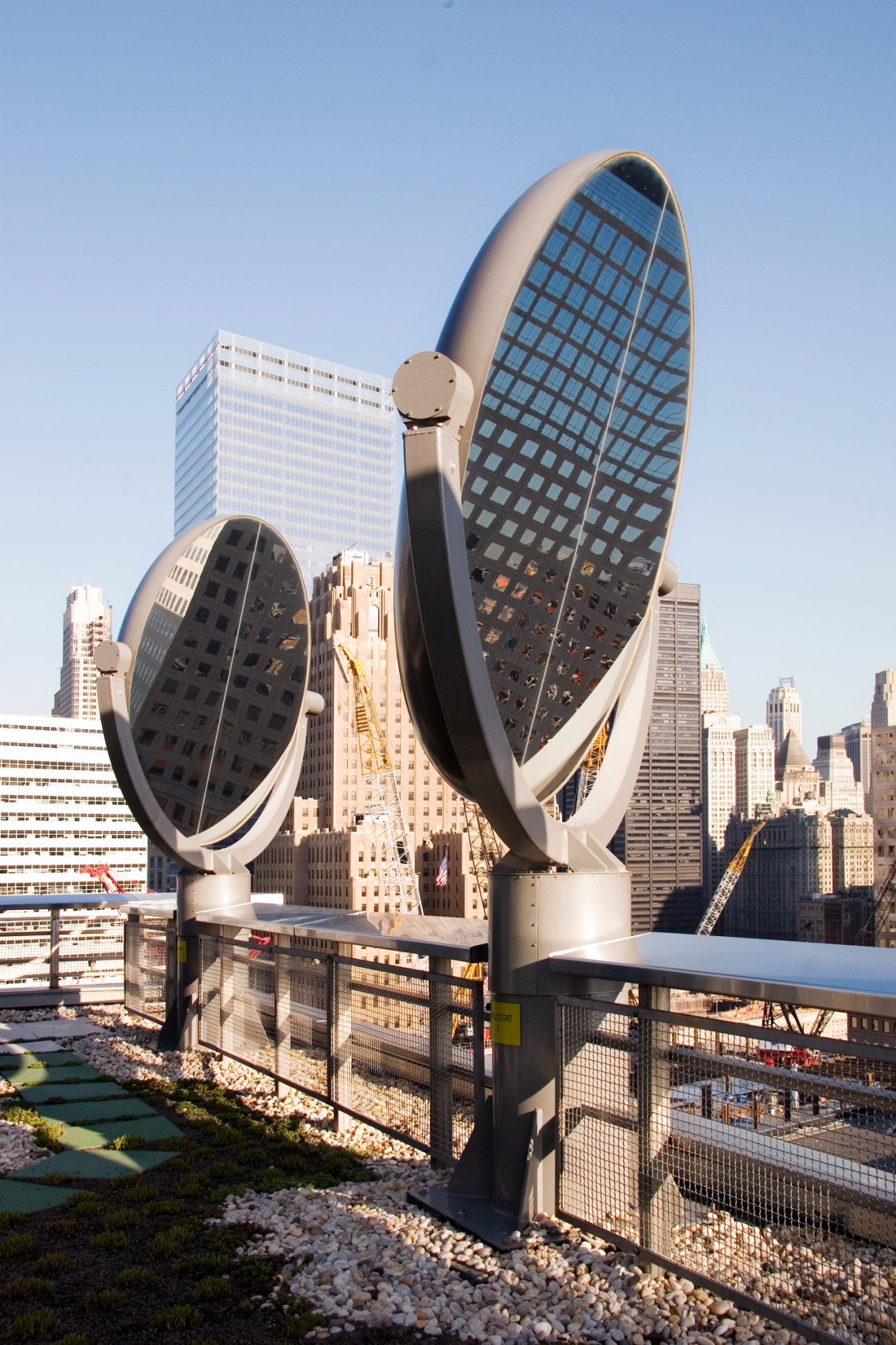 Two large metallic circular sculptures with grid patterns on a rooftop overlooking Manhattan skyscrapers.