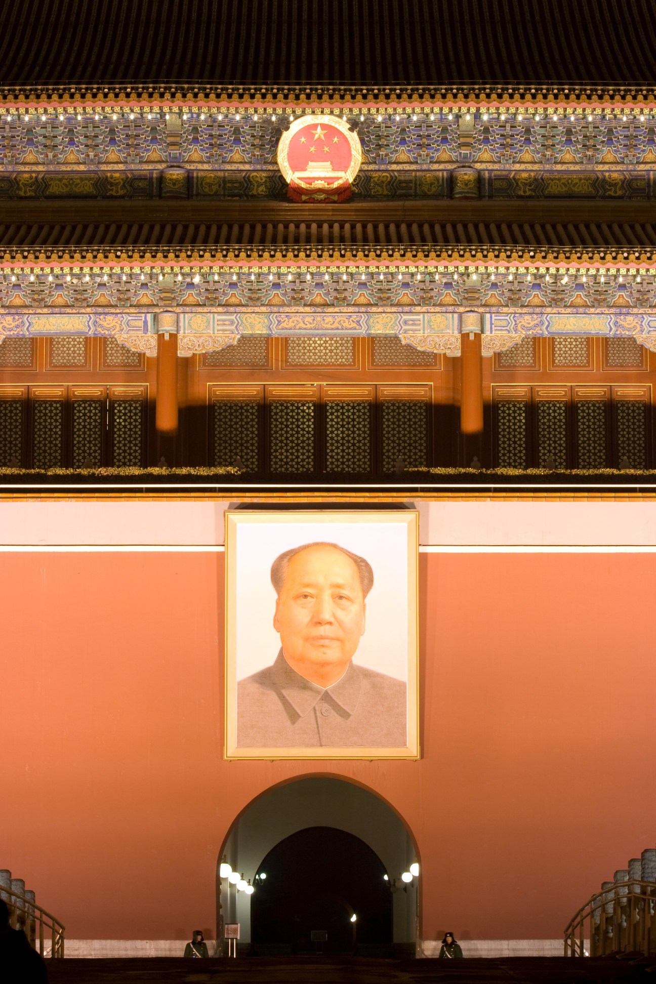 Mao Tse-tung portrait hanging on red wall below ornate traditional Chinese architecture and national emblem at Gate of Heavenly Peace.