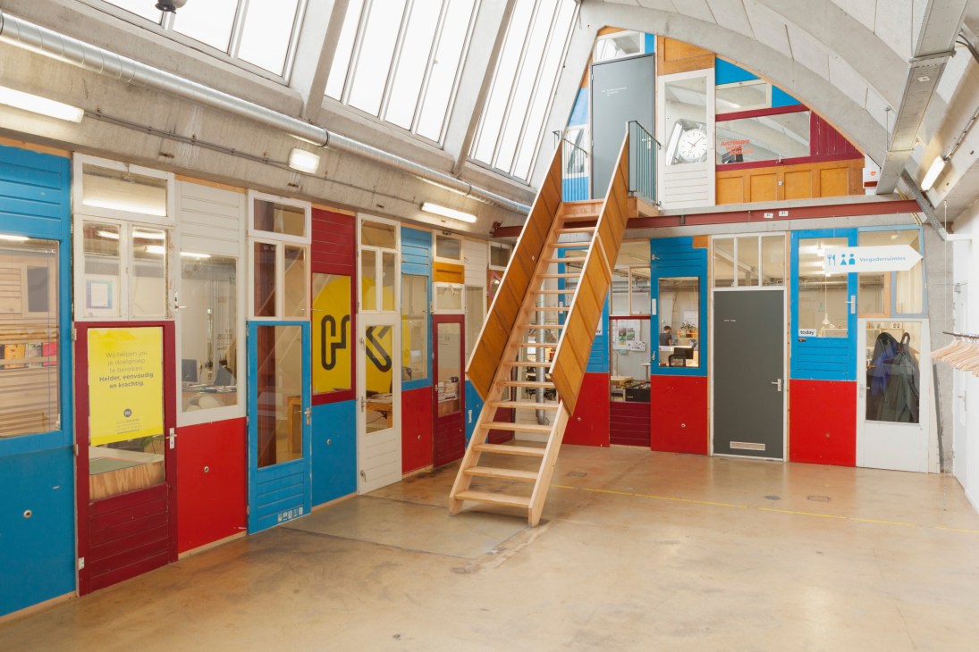 Interior workspace with colorful reclaimed doors used as partitions and wooden staircase.