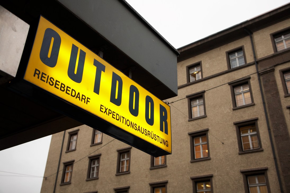 Yellow storefront sign for Outdoor Reisebedarf with tan-colored apartment building behind it.