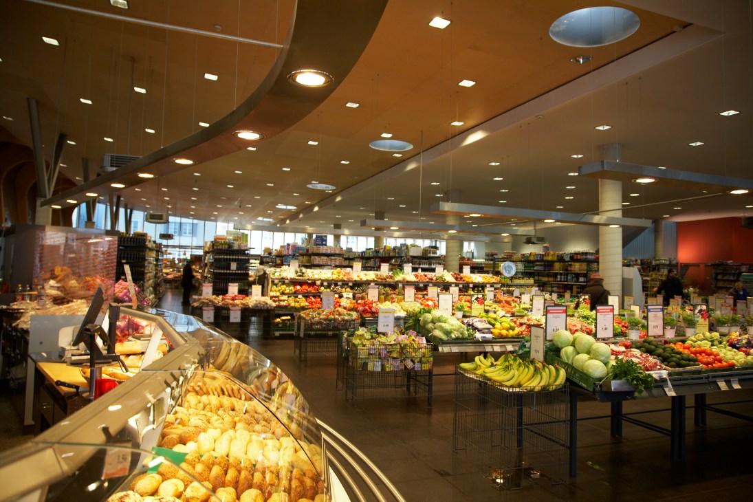 Interior of MPreis SuperM supermarket showing produce displays with fruits and vegetables under bright lighting.