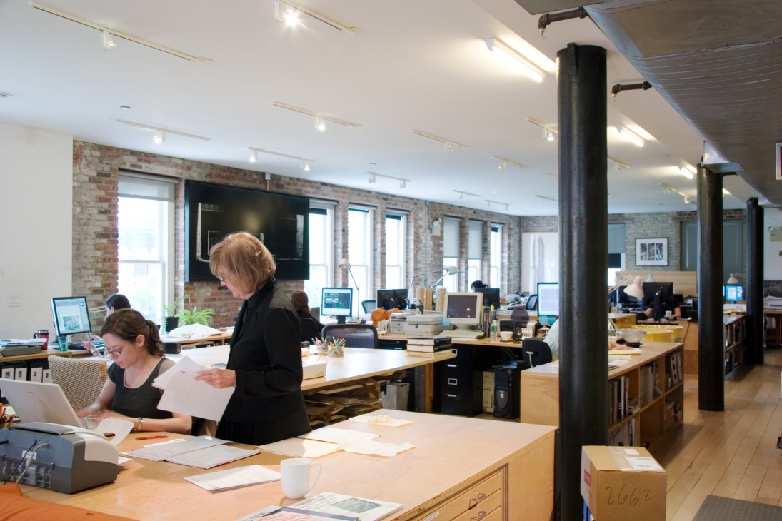 Diana Balmori stands in her loft-style Manhattan office with exposed brick walls, wooden desks, and computers.