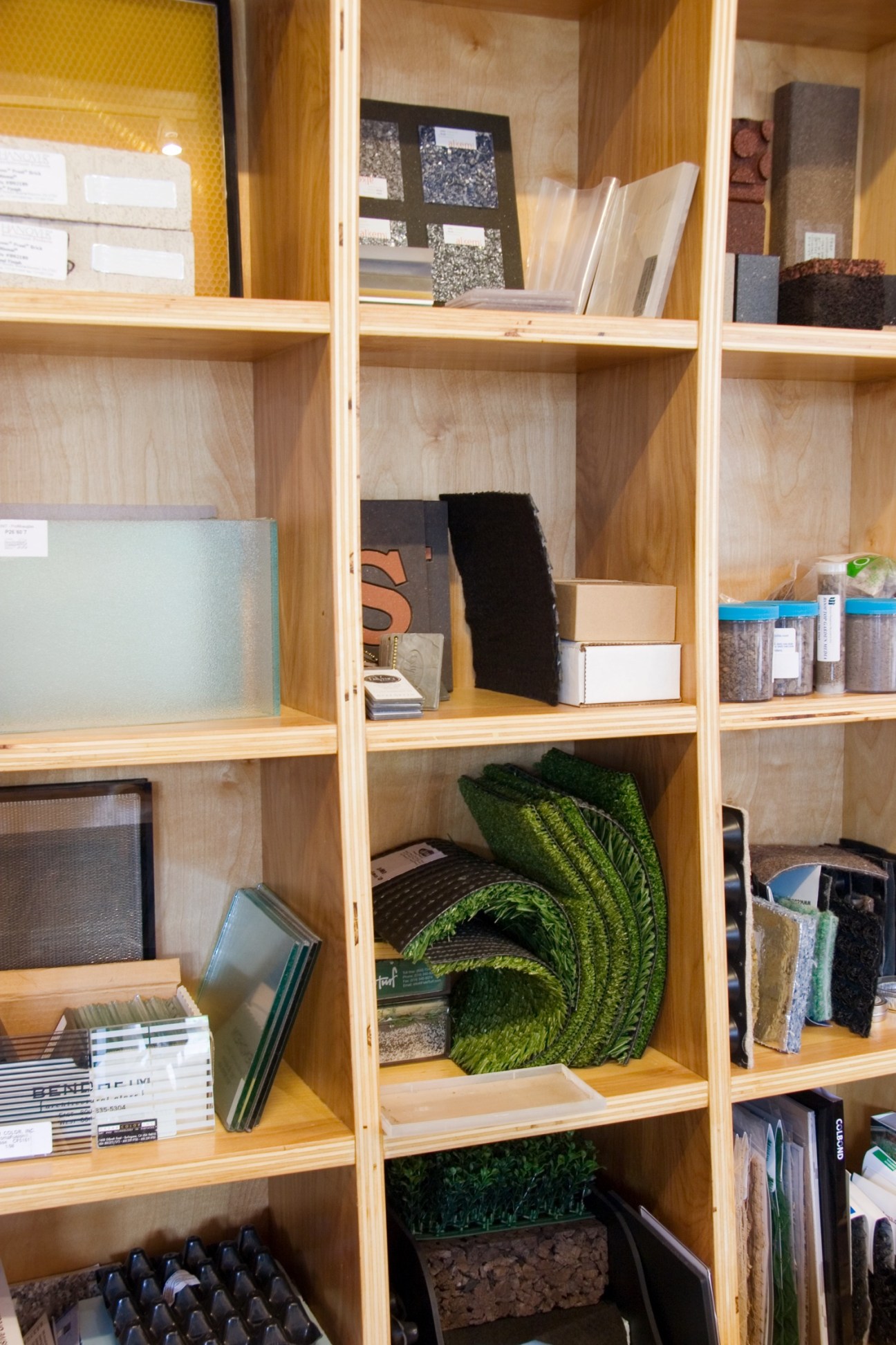 Wooden shelves displaying material samples, fabric swatches, texture boards, and design samples in Balmori Associates' office.