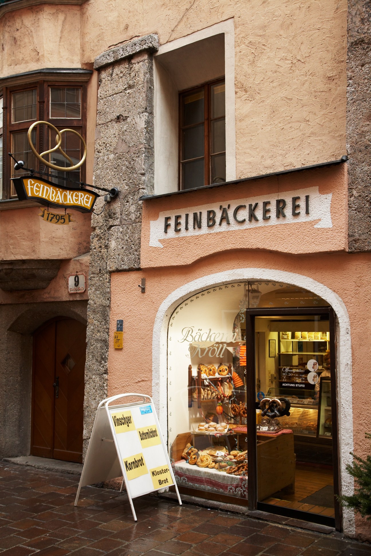 Storefront of Bäckerei Kröll bakery with peach-colored facade, wooden door, and display window showing baked goods.
