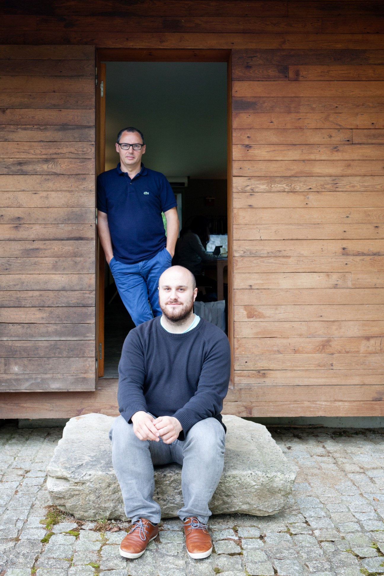 Jean Louis Iratzoki and Ander Lizaso pose outside their countryside studio in a wooden structure.