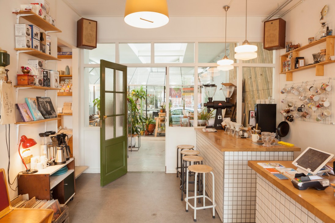 Interior of Koffie Leute Brauhaus café with wooden shelving, pendant lights, and a counter with stools.