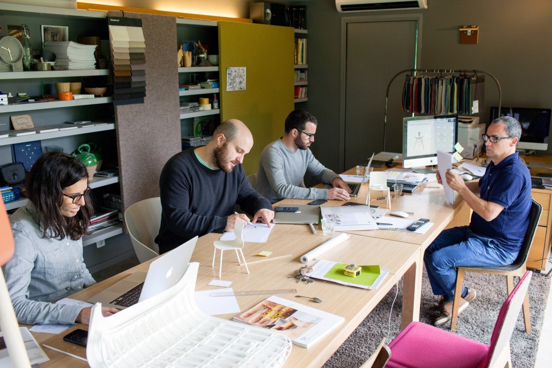 Four people seated around a wooden table in a design studio reviewing materials and sketches.