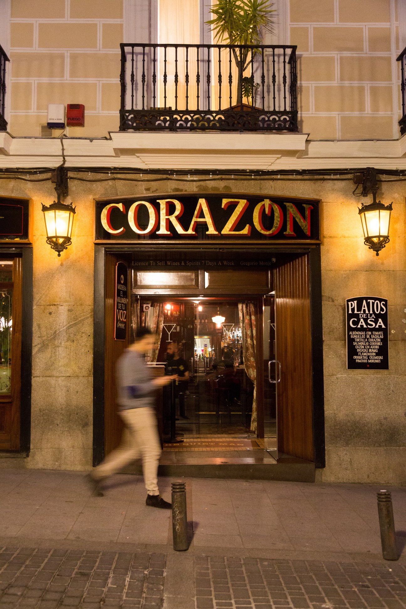 Corazón bar storefront illuminated at night with ornate balcony above, Madrid.