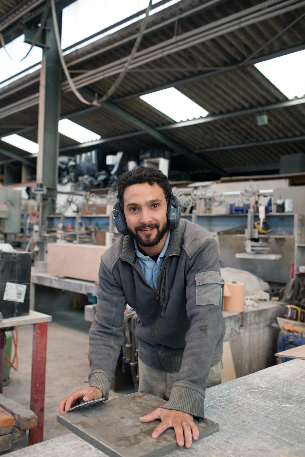 Factory worker wearing headphones at workbench in industrial furniture manufacturing facility.
