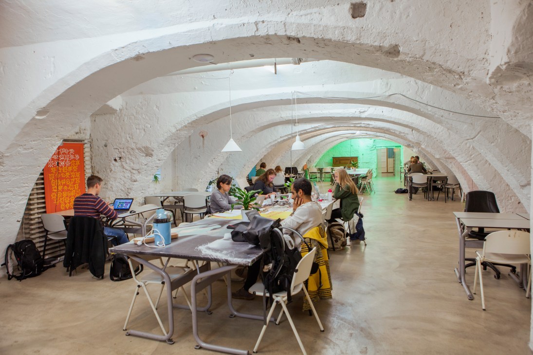People working at desks in a vaulted underground space with arched white brick ceilings.