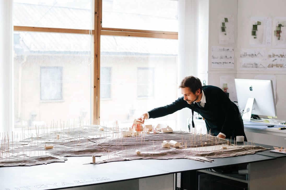 Håkon Matre Aasarød examines an architectural model of Utøya in a bright studio workspace.