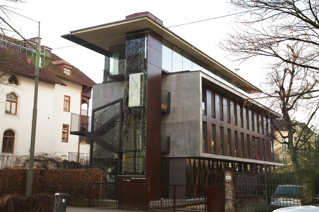 Modern apartment building with concrete and glass facade beside traditional Austrian villa in Innsbruck's Saggen district