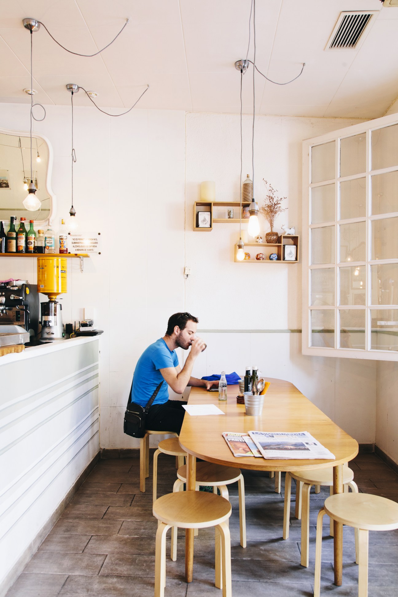 Man sitting at wooden table in minimalist café with Scandinavian furniture and white walls.