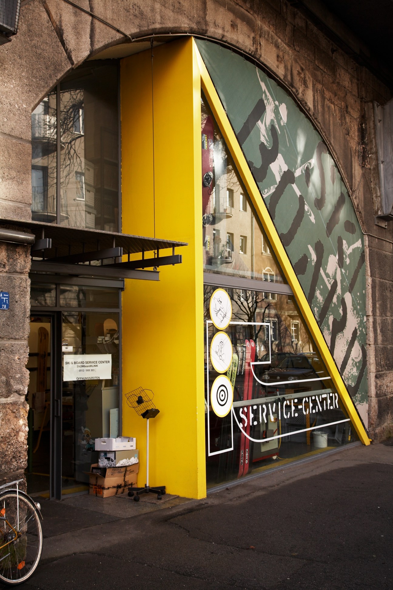 Snowboard Klinik storefront with bright yellow facade and large angled window under arched building.