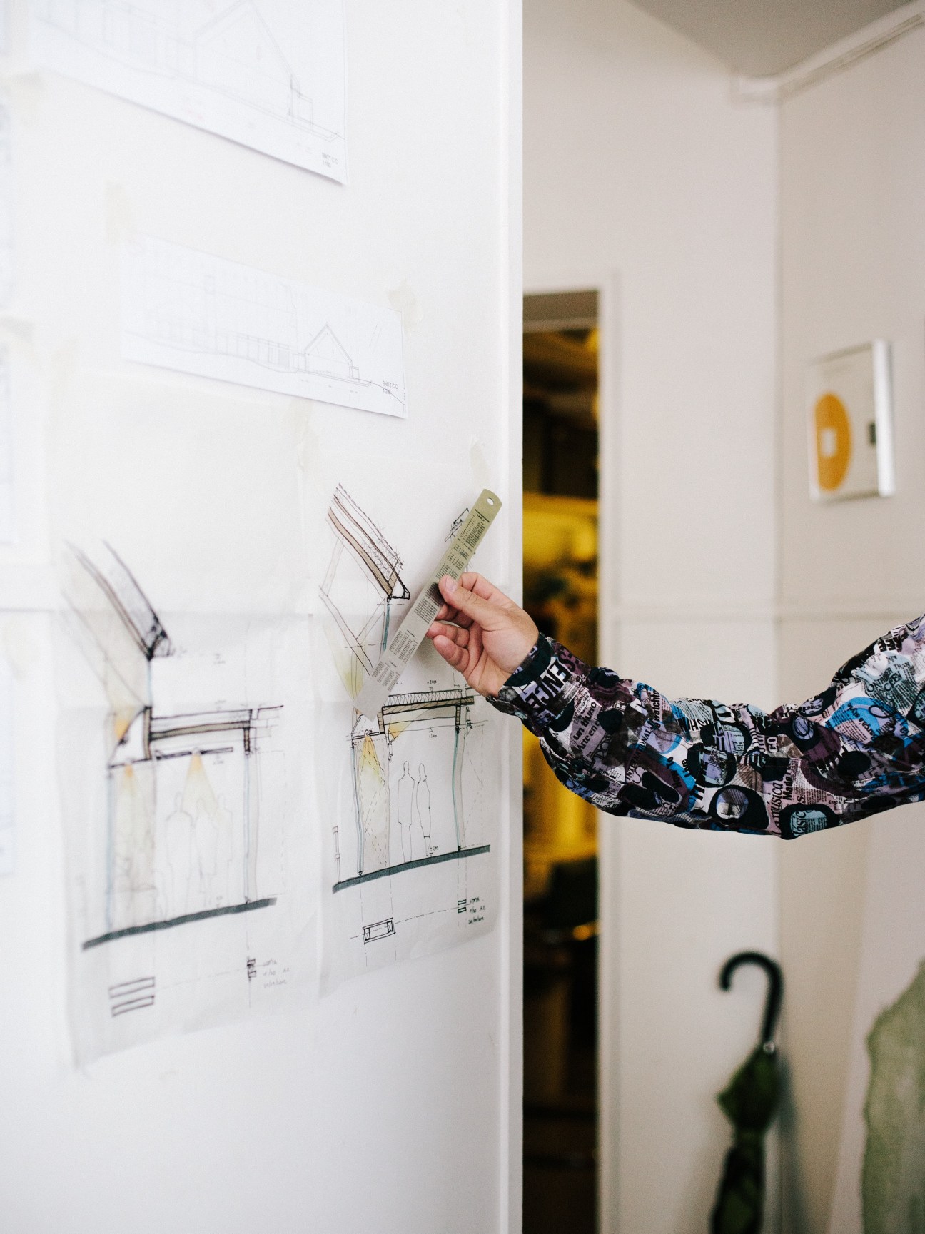 Architect's hand holding a ruler against architectural drawings pinned to a white wall.
