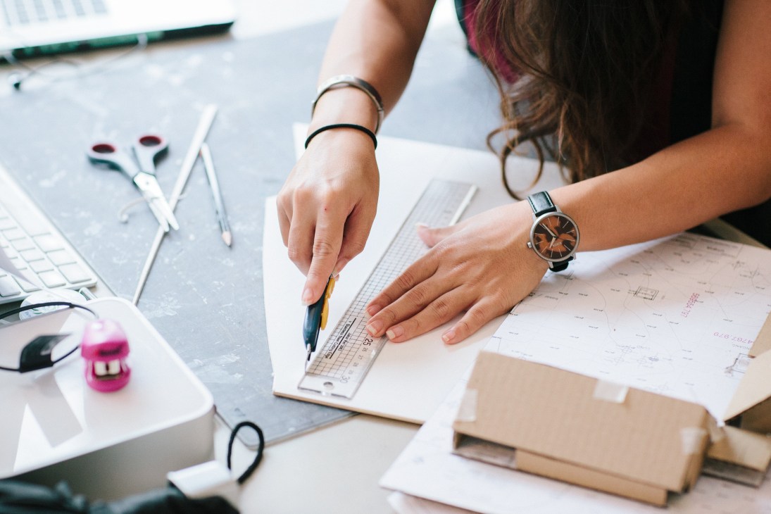 Person's hands with bracelet and watch working on architectural blueprints and design plans at a desk.