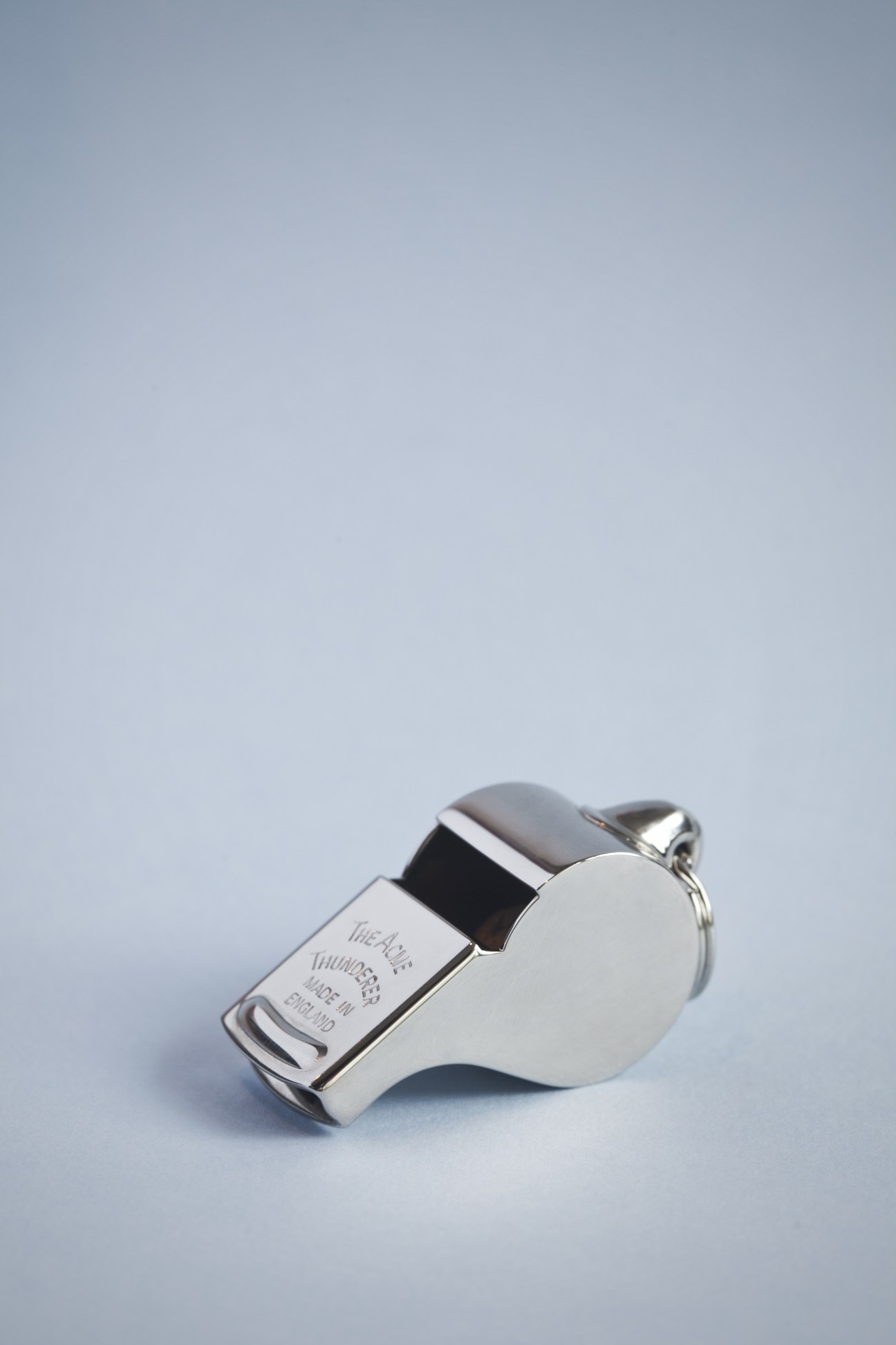 Acme metal whistle with black band and keyring against light blue background.
