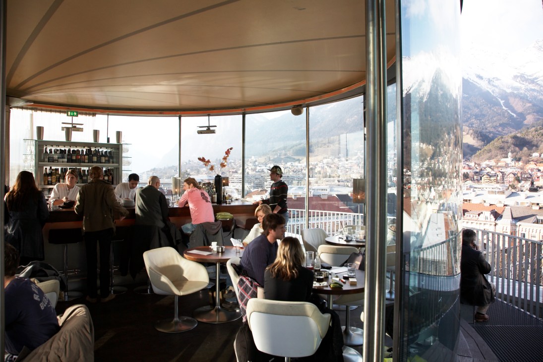 Interior of 360º bar lounge with panoramic windows overlooking Innsbruck and Alpine mountains.