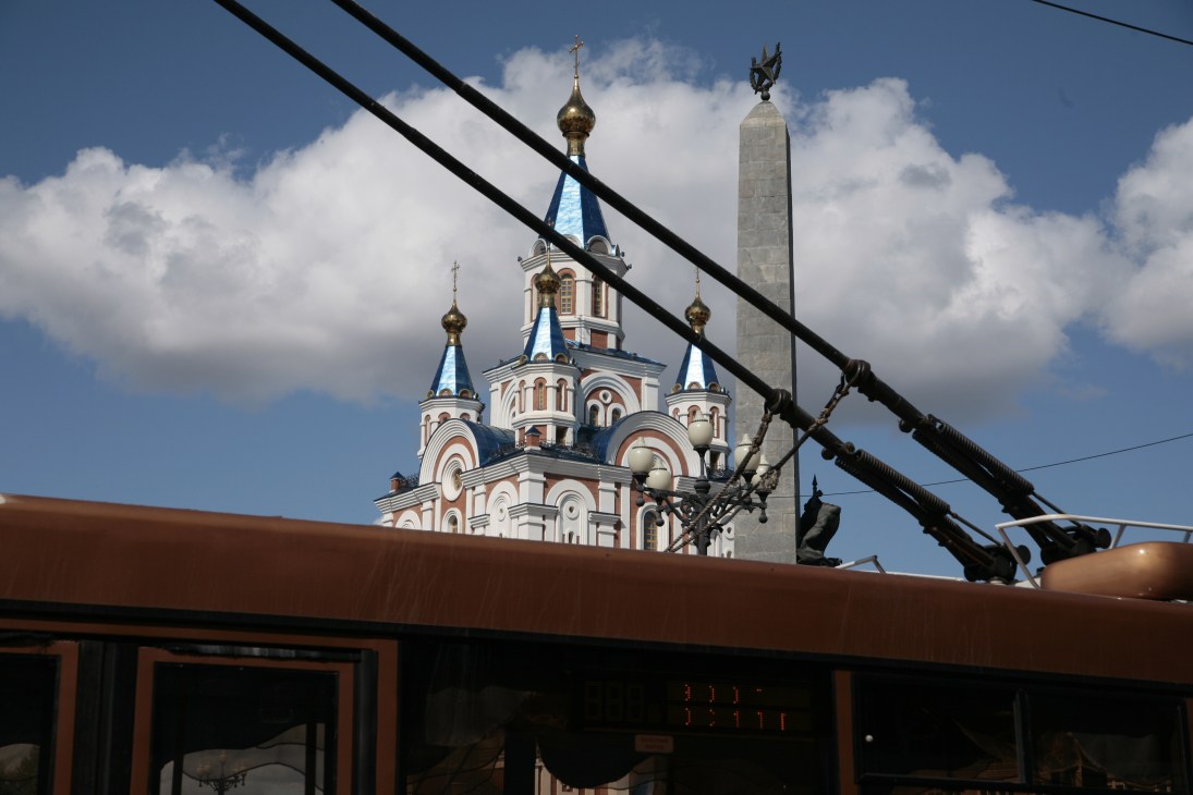 Orthodox church with blue domes and gold crosses behind power lines and modern building in Komsomolskaya Square.