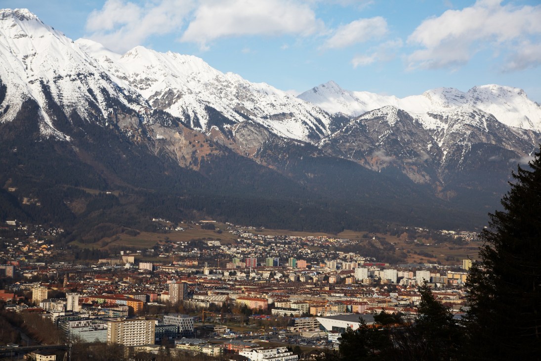 Snow-capped Alpine mountains rise behind Innsbruck's urban sprawl and apartment buildings in the valley below.
