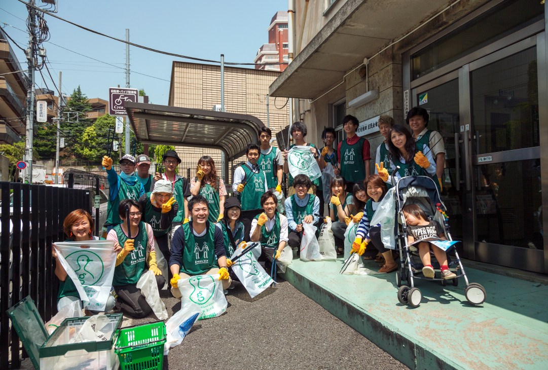 Green Bird volunteers in green bibs and yellow gloves gather on a Tokyo street before their cleanup shift.
