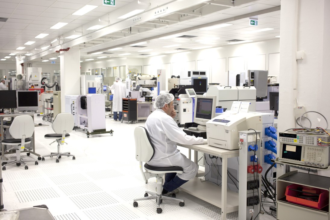 A technician works at a desk in a clean laboratory filled with testing equipment and machinery.