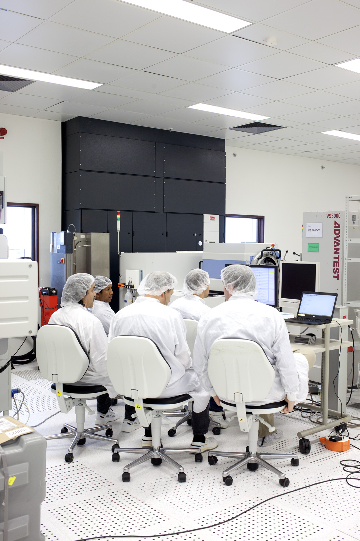 Five technicians in white coats and hairnets work at computer stations in an NXP semiconductor laboratory.
