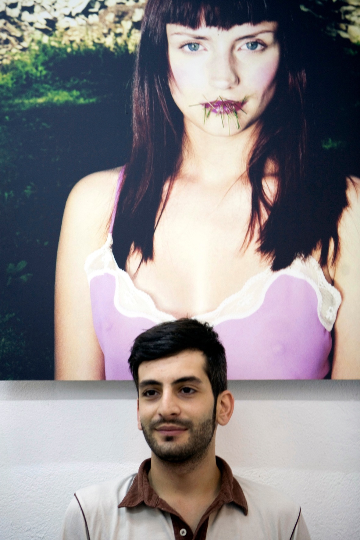 Man standing in front of a portrait photograph featuring a woman with dark hair holding a flower.