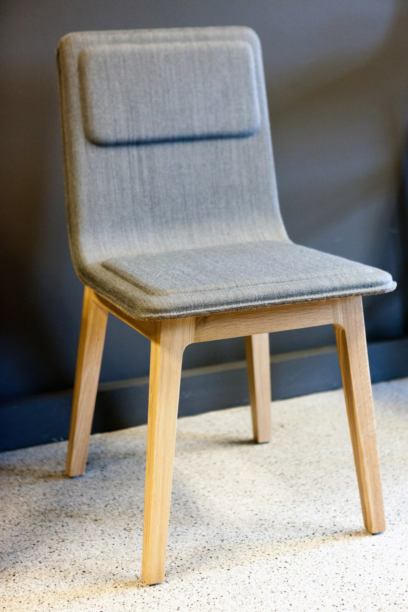 Light wood chair with gray upholstered seat and backrest on concrete floor.