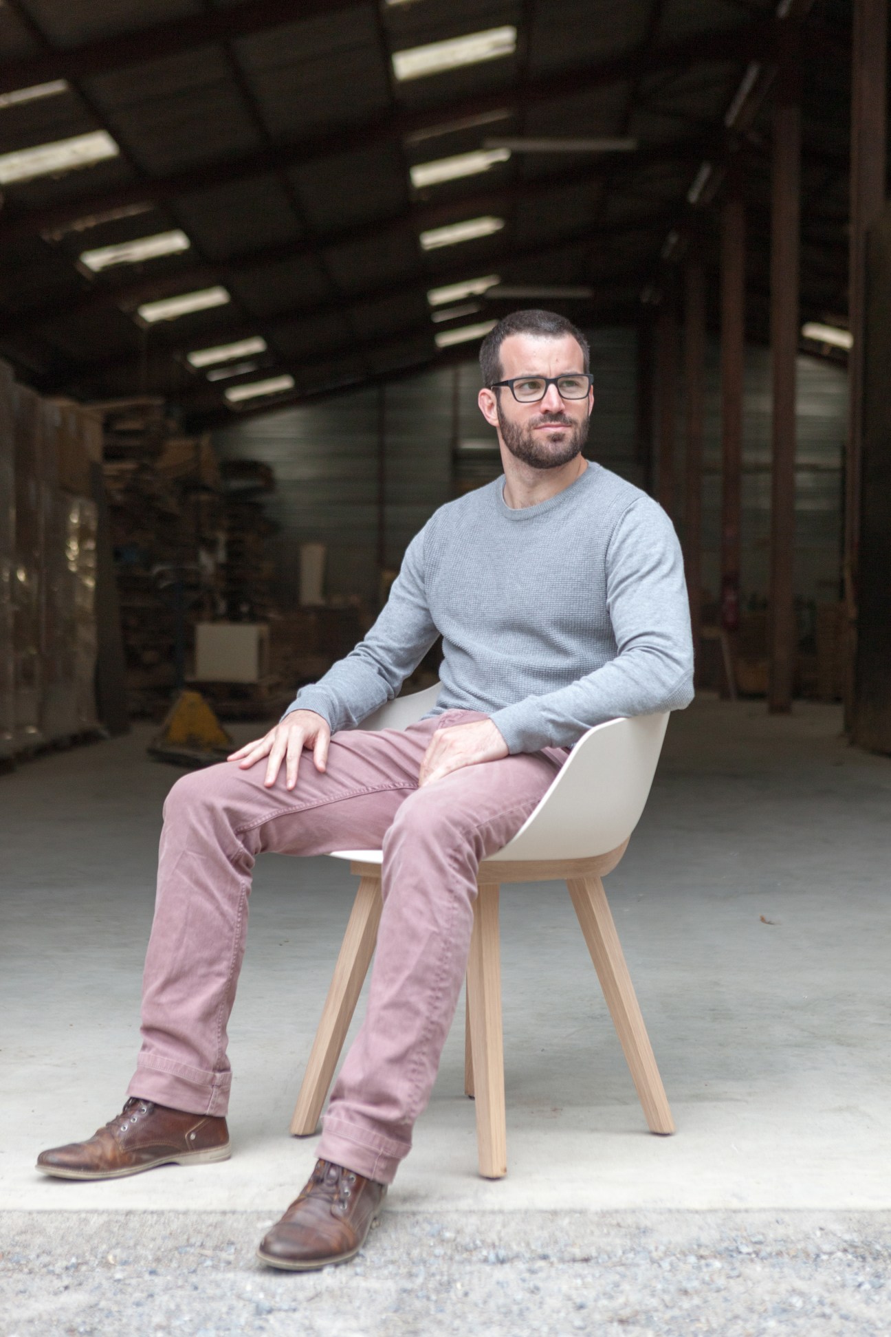 Man sitting on a light wood chair in an industrial warehouse space