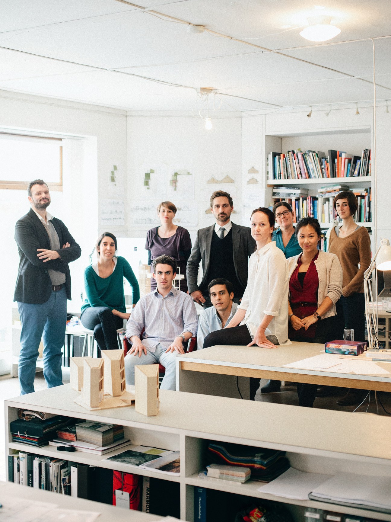 Fantastic Norway architectural team of nine people posing in their office with design drawings and bookshelves visible behind them.