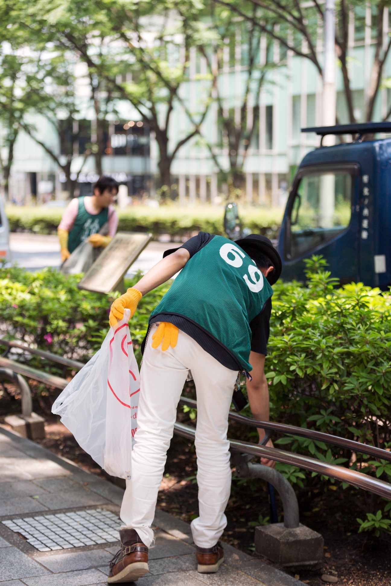 Green Bird volunteer in green vest and yellow gloves picking up litter on an urban street.
