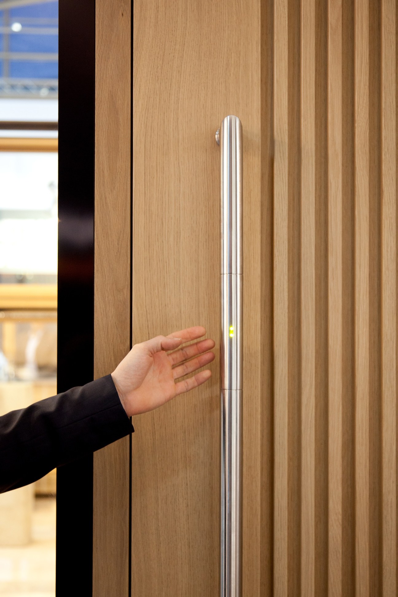 Hand touching a polished stainless steel door handle on wooden door at BAU exhibition