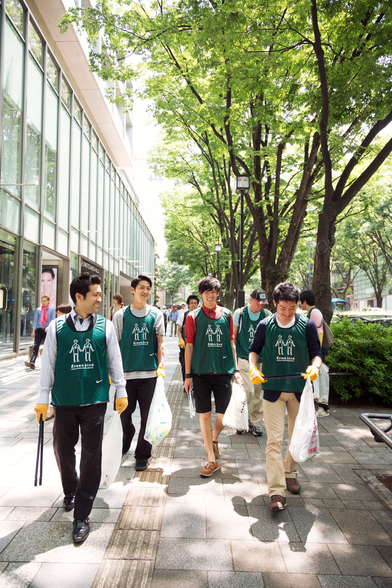 Green Bird volunteers in green vests and Nike bibs clean Omotesando street in Tokyo with tongs and bags.