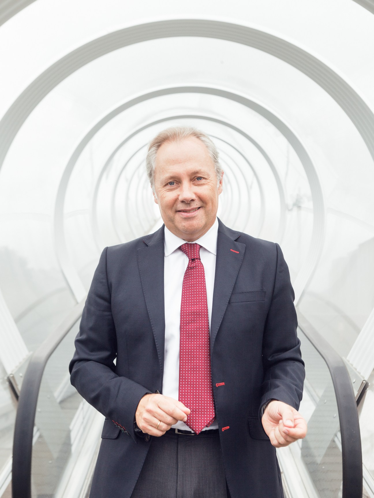 Man in dark suit and red tie standing in a white spiral tunnel structure.